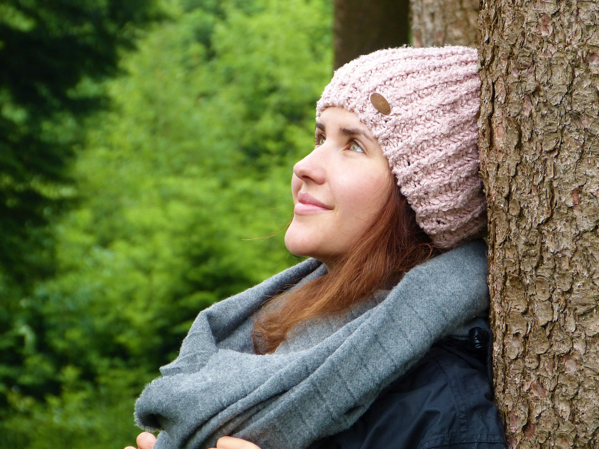 A woman in pink cap standing against a tree