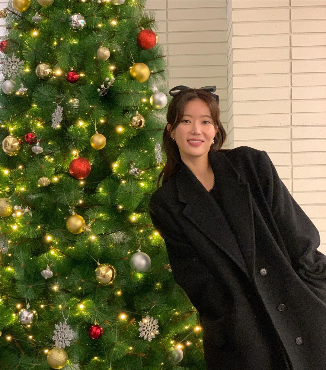 Im Soo Hyang in long black coat posing with a christmas tree