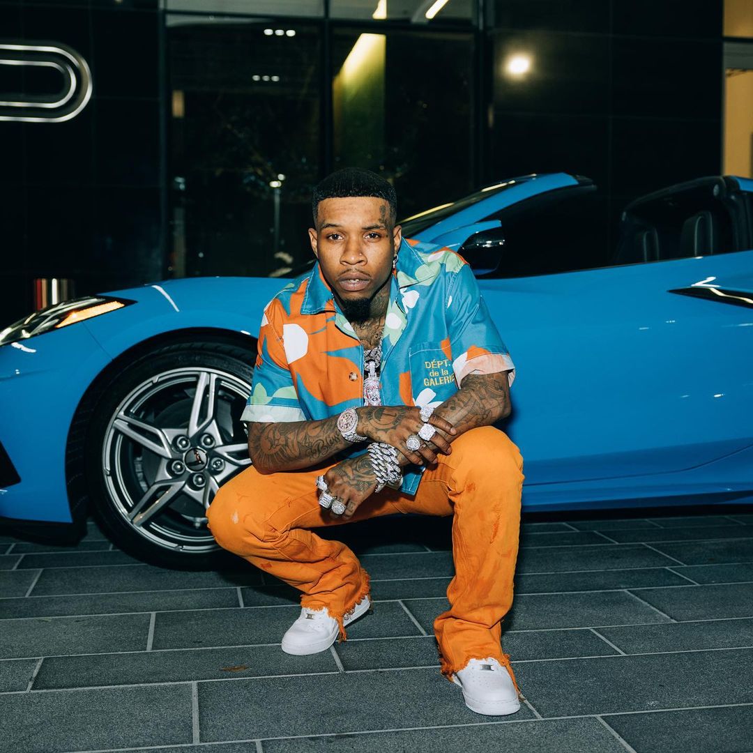 Tory Lanez posing in front of a blue Luxury car
