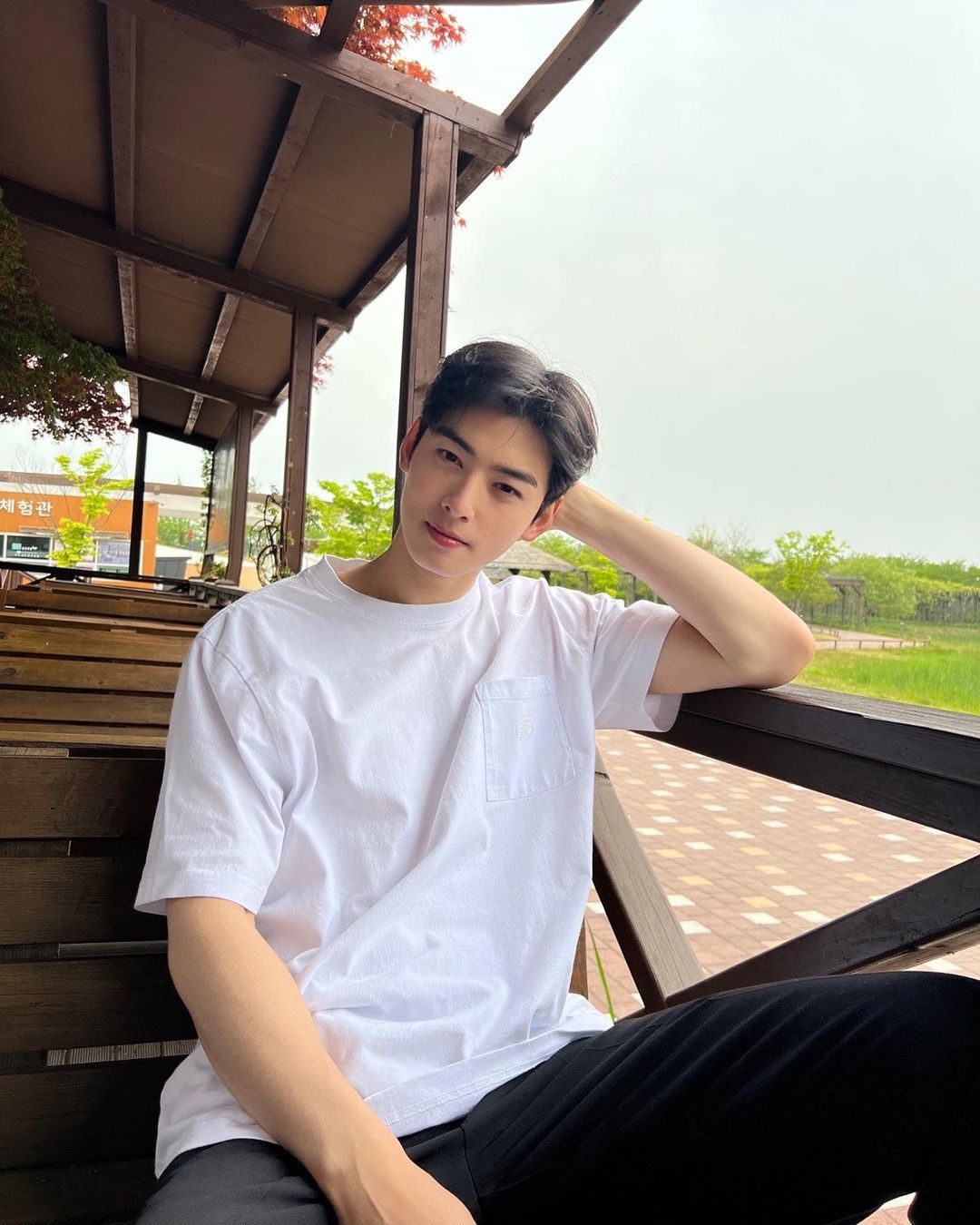 Cha Eun Woo sitting on a bench in white t-shirt and black pants