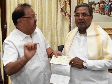 Siddharamaiah holding an official document in hand and standing with another politician